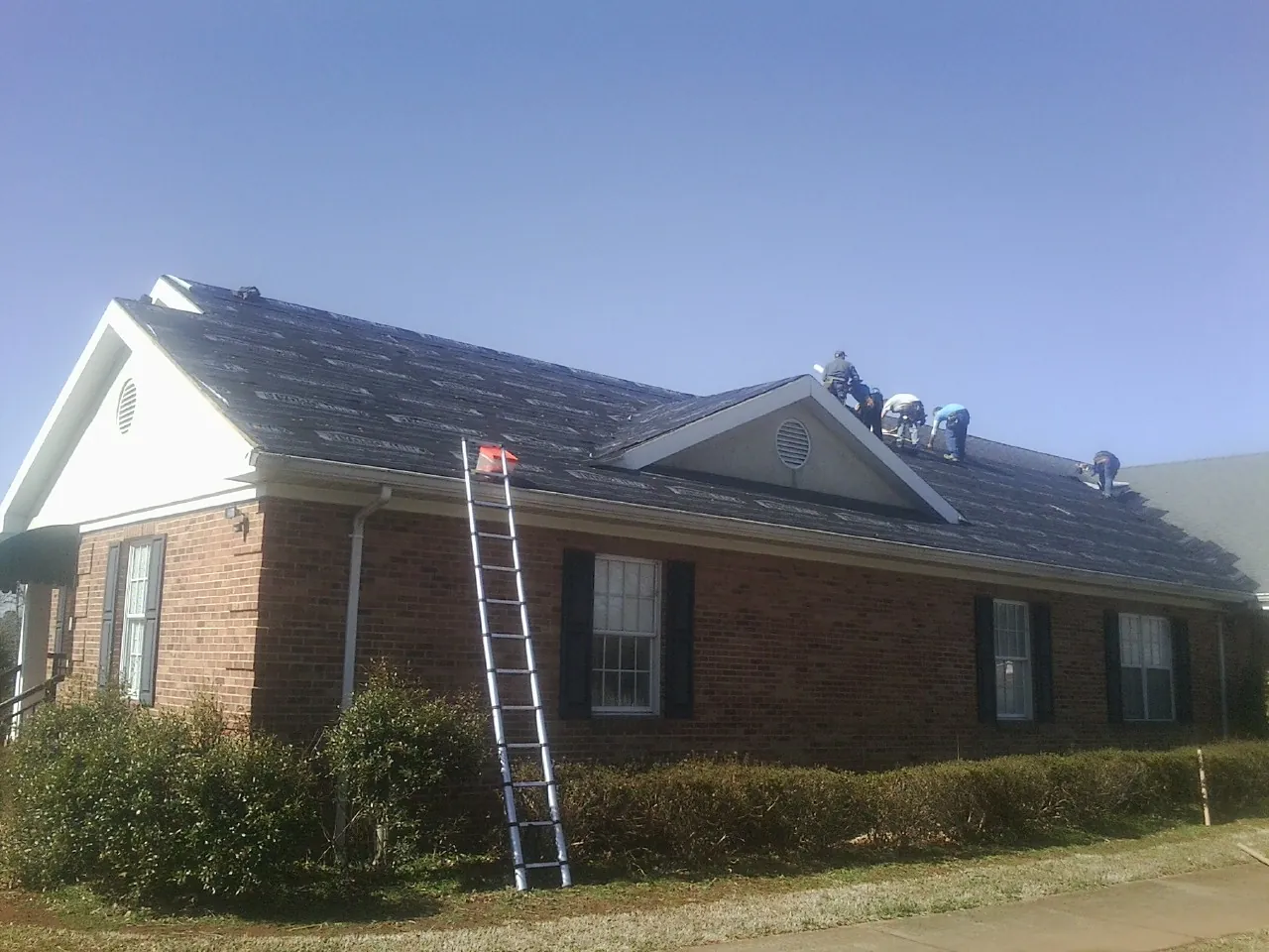 Crew tearing shingles off a brick ranch roof with a ladder set — Emergency Roof Repair work by our crew in Melcroft