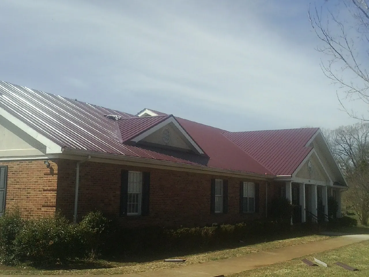 Red metal roof with gabled entries on a long brick building, from a Hail Damage Roof Repair job in Melcroft
