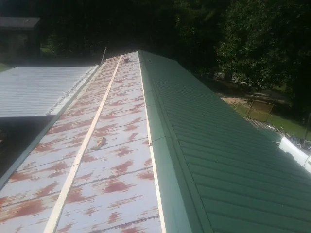 Old rusted panels beside newly installed green metal roofing — Wind Damage Roof Repair by Roofing Brothers in Melcroft