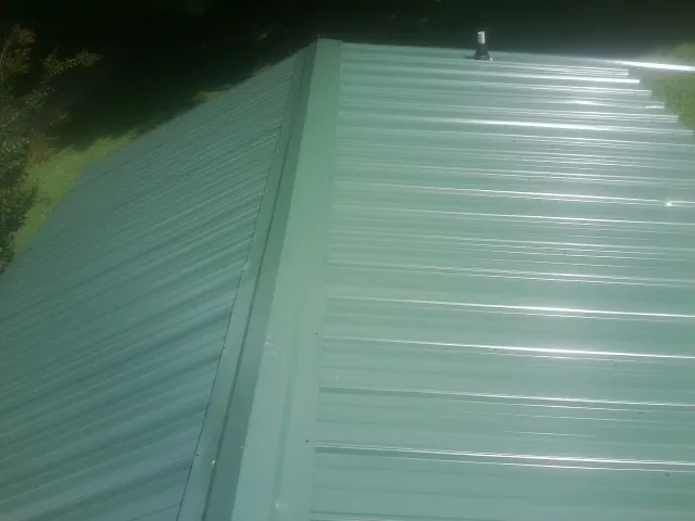 New green metal panels meeting at the ridge of a roof — Flat Roof Repair work by our crew in Melcroft