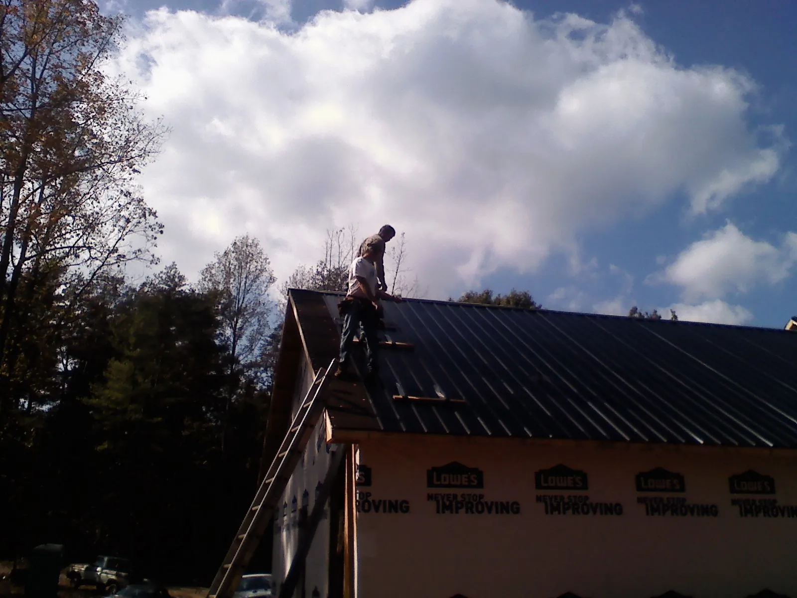 Roofer fastening dark metal panels high against a cloudy sky, from a Roof Inspection job in Melcroft