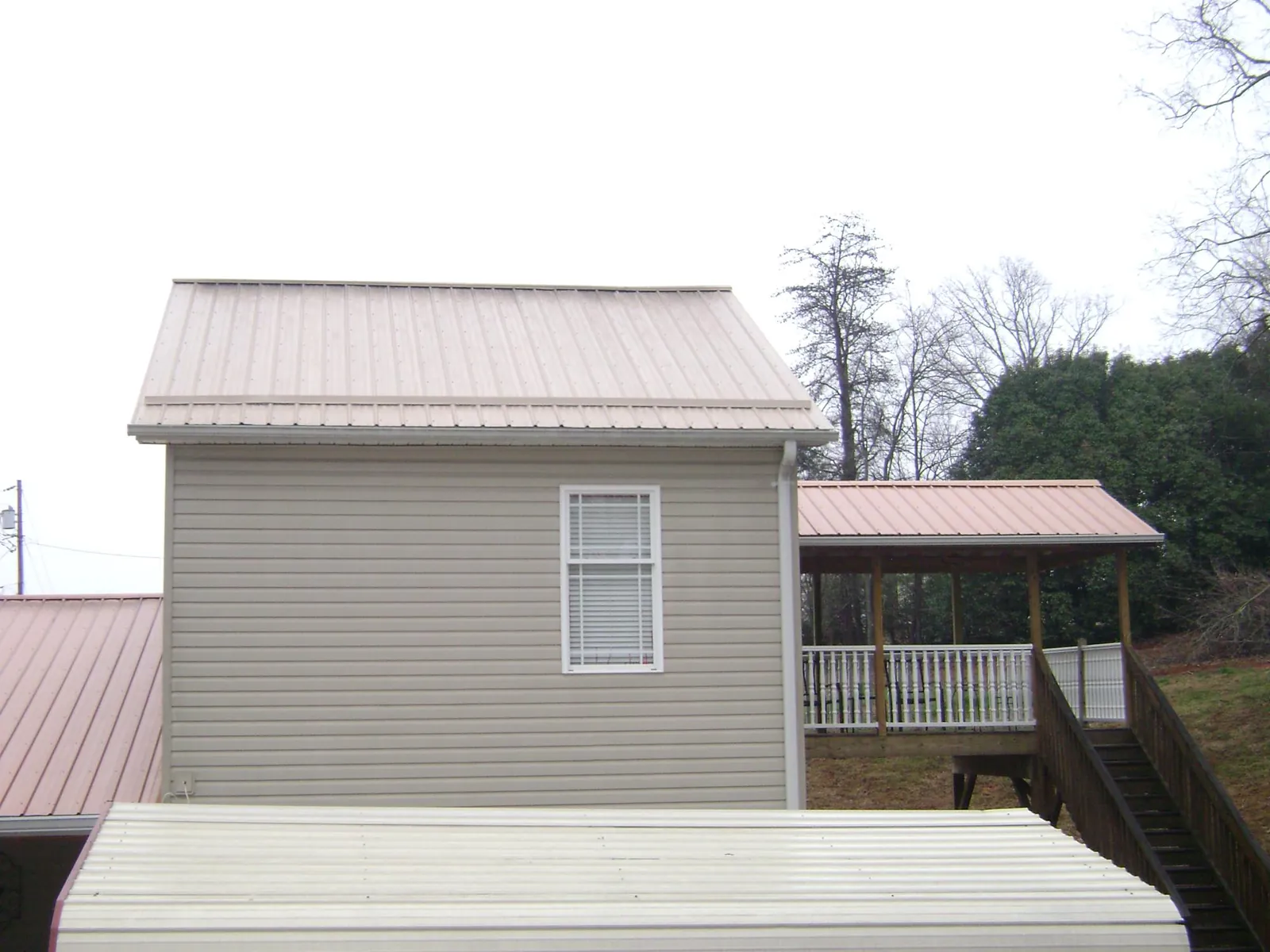 Tan metal roofs on a two story addition and attached porch, from a Roof Replacement job in Melcroft